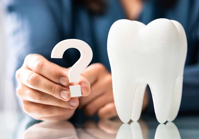 Stock photo of a man holding a question mark next to a large tooth statue